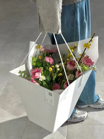 Person holding a white paper bag filled with flowers on a light gray floor.