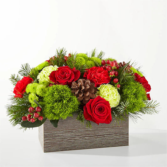 Christmas-themed floral arrangement with red roses, greenery, and berries in a wooden box on a white background.